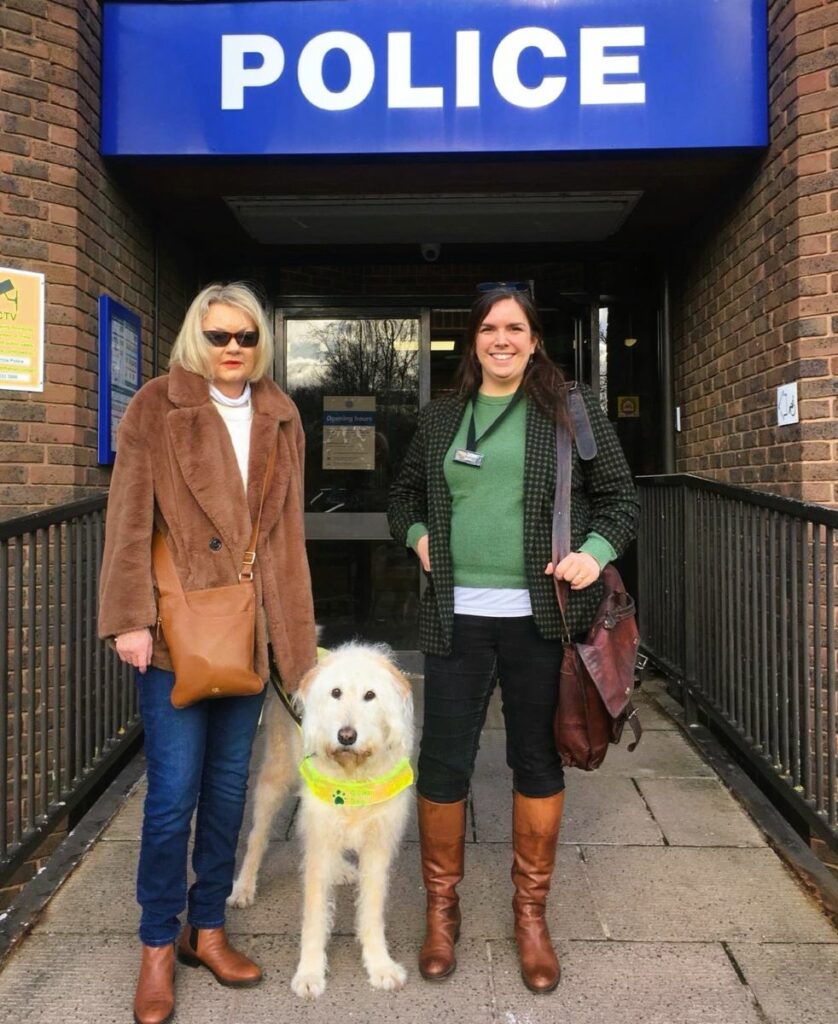 Two people and a guide dog standing outside a police station 