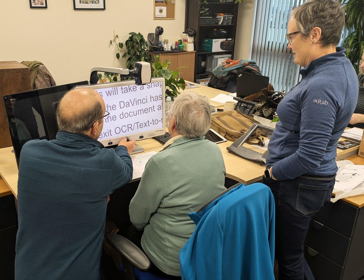Three people in the SLS office, trying out an electronic magnifier.