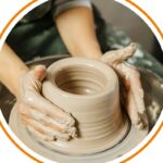 Two hands throwing a pot on a pottery wheel.