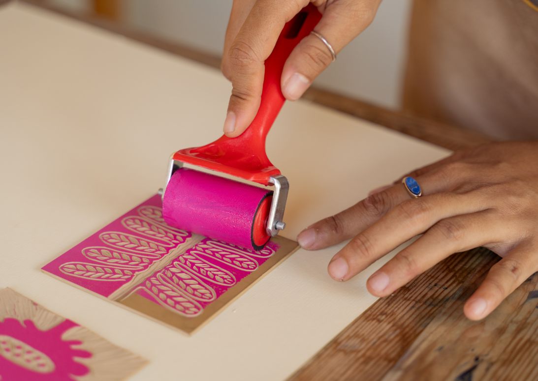Hands rolling ink onto linocut template