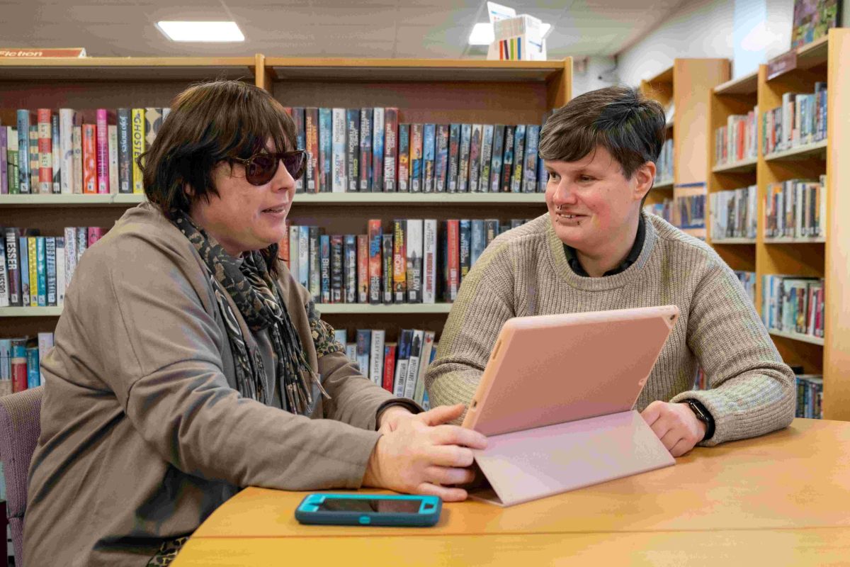 SLS – Nicky & Vicki Tech Coordinator Vicki and client Nicola meeting in a library, practising smartphone and tablet functions.