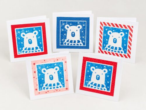 Christmas cards featuring an original linocut print of a polar bear wearing a cosy scarf against a starry sky.