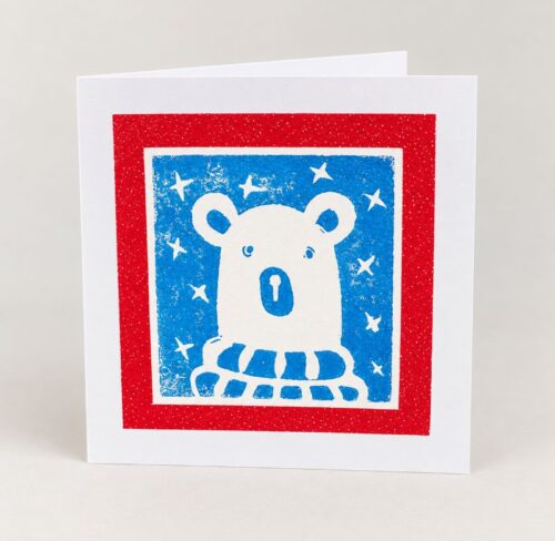 Christmas cards featuring an original linocut print of a polar bear wearing a cosy scarf against a starry sky.