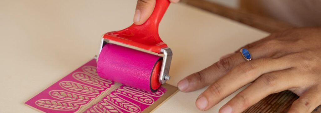 Hands rolling ink onto linocut template
